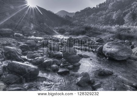 Beautiful Reshi River water flowing on rocks at dawn Sikkim India - sun rays at the background falling on water making spectacular view black and white image