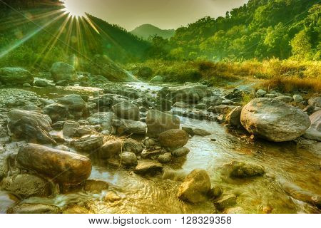 Beautiful Reshi River water flowing on rocks at dawn Sikkim India - sun rays at the background falling on water making spectacular view tinted image