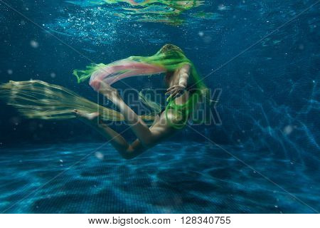 Girl swimming underwater while playing a multi-colored cloth.