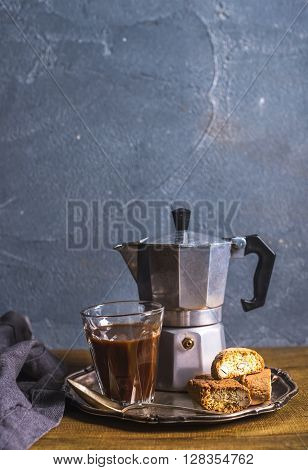 Glass espresso coffee on rustic wooden board, cantucci biscuits and steel Italian Moka pot, grey background, selective focus