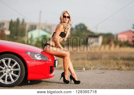 sexy girl in a black bikini sitting on a red car