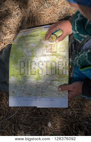 Map and compass in sunspot on the lap of a hiker who sitting on the ground. Route planning.