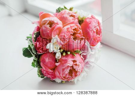 Wedding bouquet on window sill. Bride's traditional symbolic accessory. Floral composition with red celosia flowers.