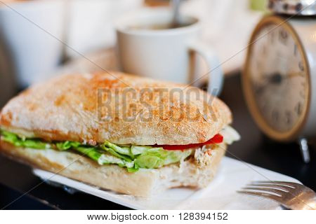 Tme for lunch with big tasty sandwich and cup of coffee.