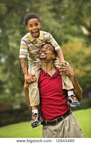 Vater mit seinem Sohn auf seinen Schultern lächelnd und Blick auf einander.