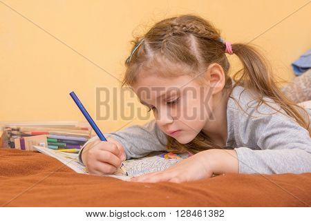 Little Girl Draws A Hard Lying On His Stomach With A Pencil On Paper