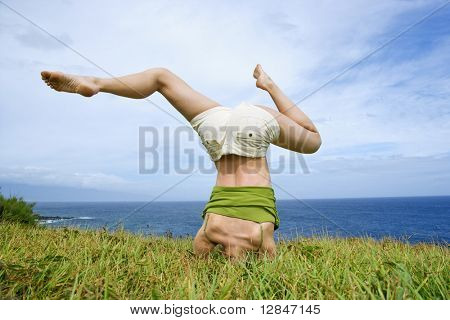Nuori nainen tekee headstand jalat askew ruoho lähellä ocean Maui, Havaiji.