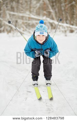 Teenage boy skis at snowy lawn in winter park.