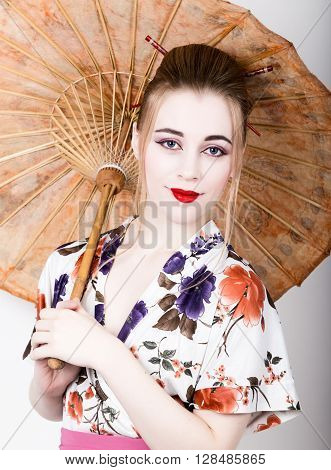 beautiful girl dressed as a geisha girl holding a Chinese umbrella. Geisha makeup and hair dressed in a kimono. The concept of traditional Japanese values.