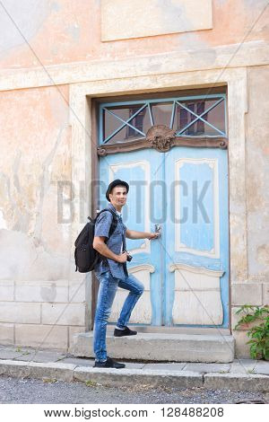 Handsome male tourist entering an old building (hostel, hotel or apartments). Traveling and couchsurfing concept.