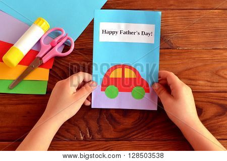 Child holds a card in his hand. Greeting card Happy father's day. Paper sheets, scissors, glue. How to make a greeting card father's day
