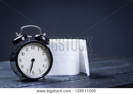 Alarm clock with toilet paper on a black wooden table