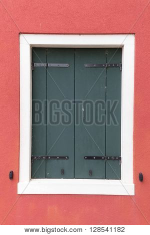 Picturesque old window with dark shutters on red wall (Burano island Venice Italy)