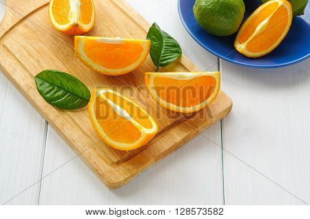 Orange segments with leaves on cutting board and white wooden surface
