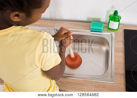 Young African Woman Using Plunger In Kitchen Sink
