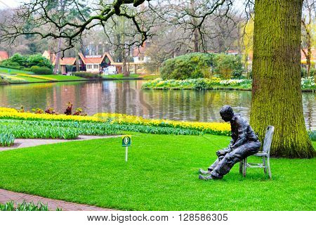 Lisse, Netherlands - April 4, 2016: Statue of man, lake, flower bed with yellow daffodil flowers in Keukenhof, Lisse, Netherlands