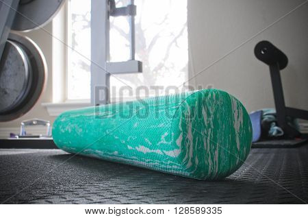 Fitness foam roller sitting on indoor gym floor with weights in background.