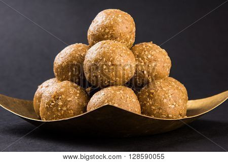 The indian sesame sweet or tilgul laddu, made up of jaggery and sesame seeds, hand made, round, indian sweet prepared in Makar Sankranti festival, served in a square brass plate, top and isolated