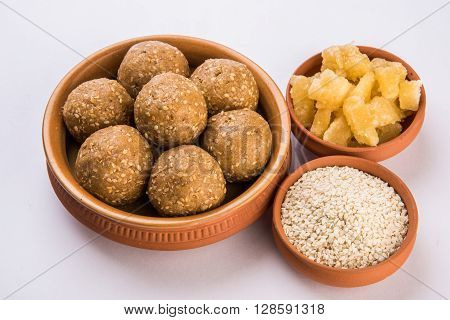 The indian sesame sweet or tilgul laddu or til gul laddu, made up of jaggery and sesame seeds, indian sweet for Makar Sankranti festival, in terracotta bowl with jaggery & raw sesame, isolated on white background