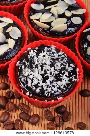 Homemade delicious fresh baked chocolate muffins with desiccated coconut and sliced almonds in red silicone cups and coffee grains on wooden background concept for dessert