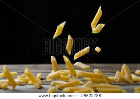 Falling penne pasta. Flying yellow raw macaroni over black background.