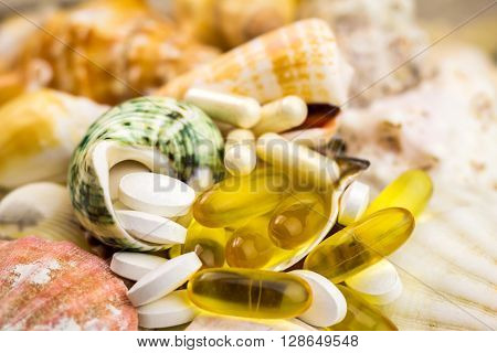 Mixed natural food supplement pills on the beautiful seashells background omega 3 calcium glucosamine capsules