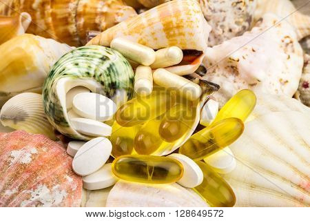 Mixed natural food supplement pills on the beautiful seashells background omega 3 calcium glucosamine capsules