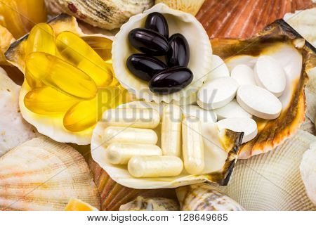 Mixed natural food supplement pills on the beautiful seashells background omega 3 calcium carotene glucosamine capsules
