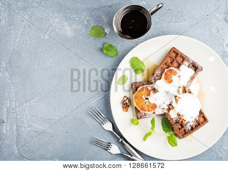 Belgian soft waffles with blood orange, cream, marple syrup and mint  on white plates over concrete textured background. Top view, copy space
