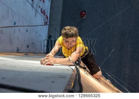 Elderly Female Climber Makes Hard Move on Outdoor Climbing Wall Sport Competitions High Up above Ground Belaying People on Remote Background