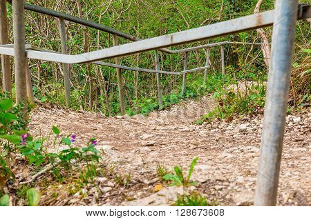 Mountain forest trail with fence and gravel leading down closeup