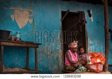 Sierra Leone, Port Loko, West Africa - June 2, 2013: the beaches of the Bunce Island, the grandmother with her grandson in front of their house on the harbor front, the heart drawn on the wall symbolizes good luck