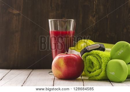 Fitness or diet concept: dumbbells, fresh red smoothie, apple, towel and activity tracker over wooden background. Toned image. Selective focus