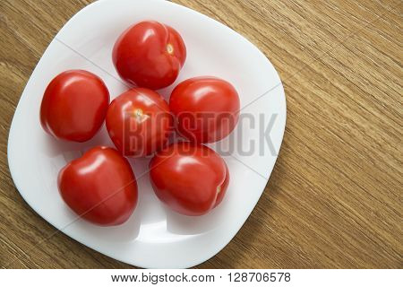 Fresh red tomatoes in white plate on wooden table