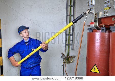 Electrician Engineer impose earth connection on reducing power transformer using Grounding Equipment discharge stick and earthing clamps cables.