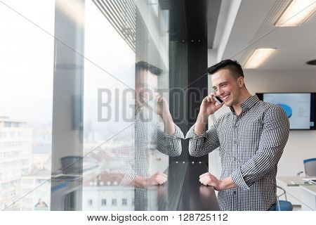relaxed young businessman speaking on smart phone at modern startup business office meeting room  with big window and city in backgronud
