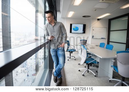 relaxed young businessman using smart phone at modern startup business office meeting room  with big window and city in backgronud