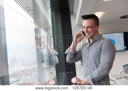 relaxed young businessman speaking on smart phone at modern startup business office meeting room  with big window and city in backgronud