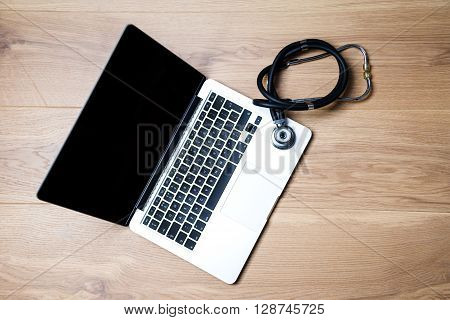 Top view of laptop with blank screen and stethscope next to it on wooden desktop. Mock up