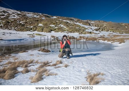 brunette woman with green red and brown clothes crouching looking to camera as photographer taking photo picture in Gredos mountain Avila Spain Europe