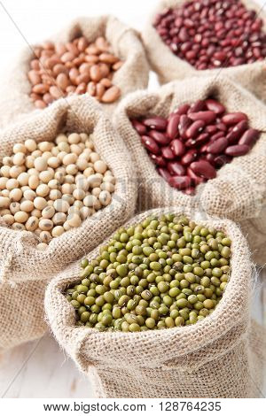 Assortment Of Beans And Lentils In Hemp Sack On Wooden Background. Green Bean, Groundnut, Soybean, R