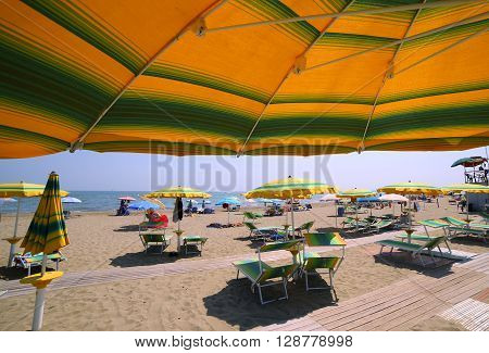 Under The Yellow With Green Stripes Umbrella On The Sunny Beach
