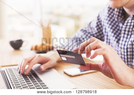 Online shopping and payment concept with caucasina male at desk typing on computer keyboard and holding a credit card