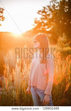 Portrait of young modern girl on the background of nature. Young woman  on a background sunset. Young woman in ripped jeans. in sun glasses