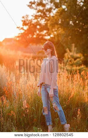 Portrait of young modern girl on the background of nature. Young woman  on a background sunset. Young woman in ripped jeans. in sun glasses