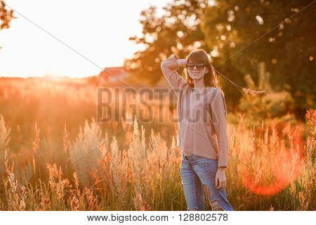 Portrait of young modern girl on the background of nature. Young woman  on a background sunset. Young woman in ripped jeans. in sun glasses