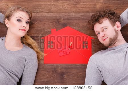 Housing marriage family security future finances mortgage concept. Just married lying on floor. Young man and woman next to home symbol with keyring.