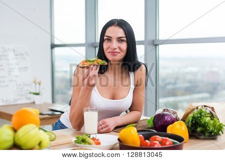 Close-up portrait of smiling woman eating diet vegetarian sandwich with vegetables for breakfast in morning, looking at camera
