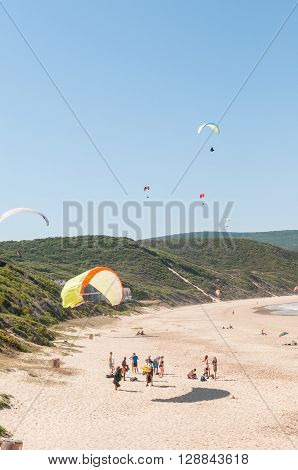 KNYSNA SOUTH AFRICA - MARCH 3 2016: Paragliders in the air while beachgoers enjoy the sun at a beach in Buffelsbaai (Buffalo Bay) a small town in the Knysna municipal area