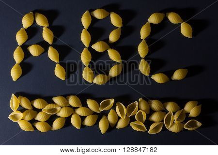 English alphabet laid out in the form of pasta shells , shot against a dark background.